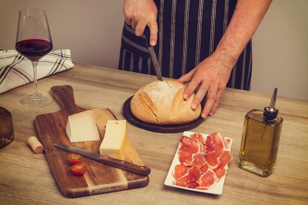 Homme coupant une miche de pain sur une table en bois avec un apéritif