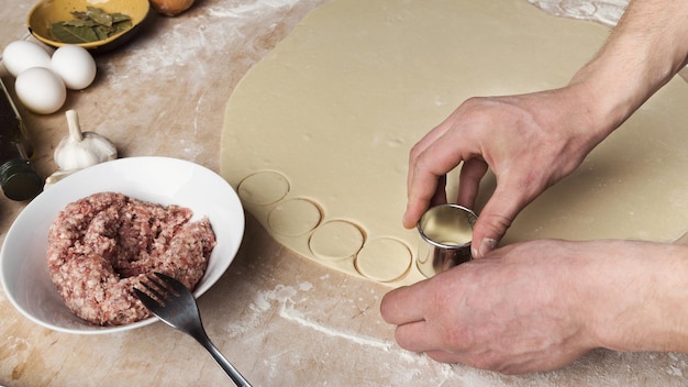 Homme coupant la pâte en petits cercles, préparant des boulettes de viande. Cuisine ukrainienne traditionnelle