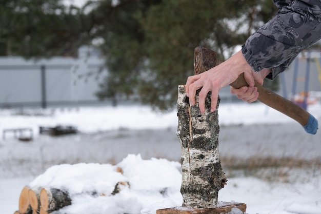 Un homme coupe du bois de chauffage avec une hache en hiver à l'extérieur dans la neige Chauffage alternatif récolte du bois crise énergétique
