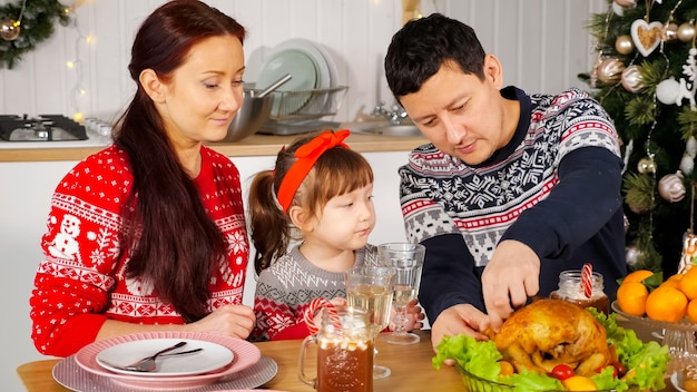 Un homme coupe du poulet pour nourrir sa famille assise à une table de vacances