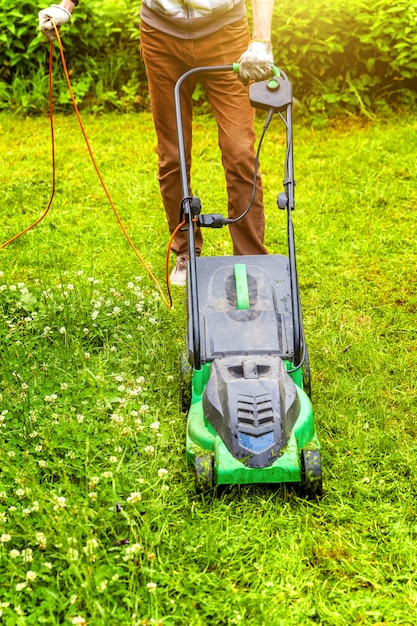 Homme coupe l'herbe verte avec une tondeuse à gazon dans l'arrière-cour. Fond de style de vie pays jardinage.