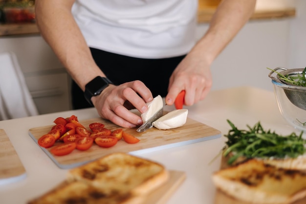 Un homme coupe de la mozzarella sur une planche de bois pour préparer un sandwich classique italien.