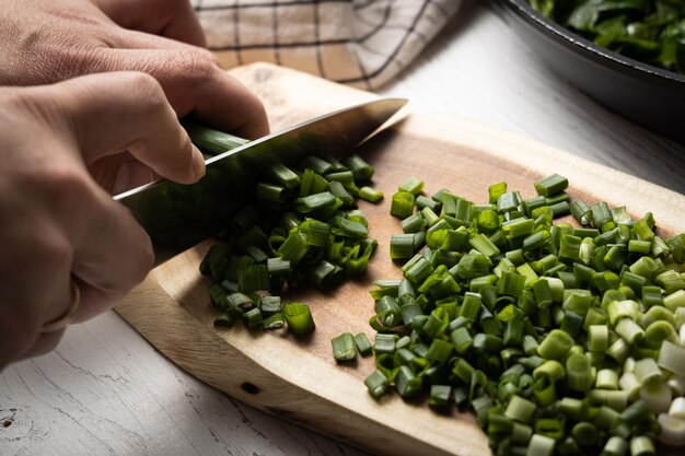 Un homme coupe des oignons verts sur une planche de bois