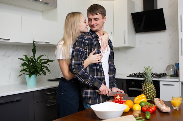 Homme coupe salade de légumes Femme embrassant son homme par derrière