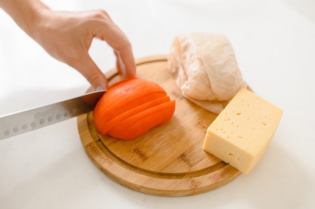 Un homme coupe les tomates sur une planche à découper dans une cuisine lumineuse.