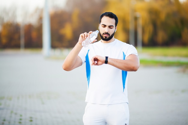 Homme coureur épuisé boire de l'eau sur le parc après l'entraînement