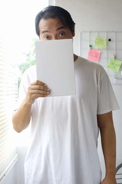 Homme couvrant son visage avec un livre blanc pour une maquette de livre sur fond blanc