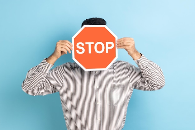 Homme couvrant le visage avec le symbole Stop personne anonyme tenant un panneau de signalisation rouge avertissant d'aller