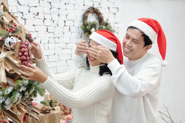 Homme couvrant les yeux de la femme décorant l'arbre de Noël pour la célébration