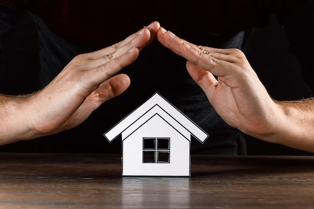 Homme couvre une maison de papier avec ses mains