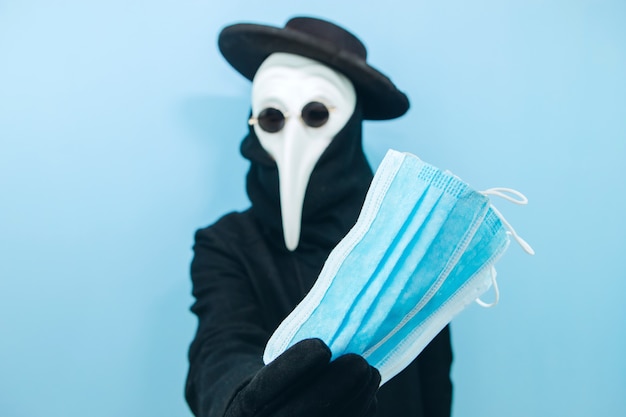 Homme créatif dans un masque de protection, des lunettes et un chapeau sur fond bleu. Protection contre les coronavirus. Epidemic covid-2019. le gars dans le masque du médecin de la peste.