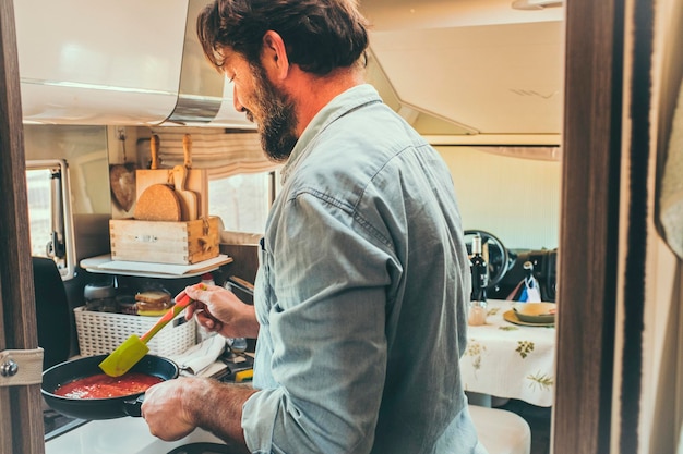 Homme cuisinant dans une cuisine de camping-car à l'intérieur. Mode de vie des gens de vacances de voyage de vacances. Adulte caucasien mâle cuire des tomates dans l'intérieur de la voiture de camping camping-car