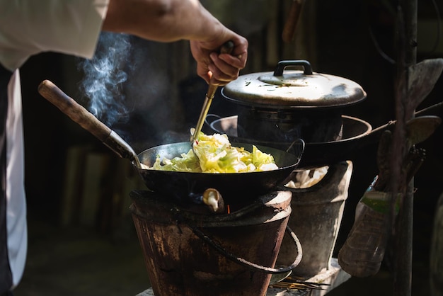 L'homme cuisinant des légumes dans une poêle à frire sur une cuisinière vintage cuisinant avec du bois de chauffage