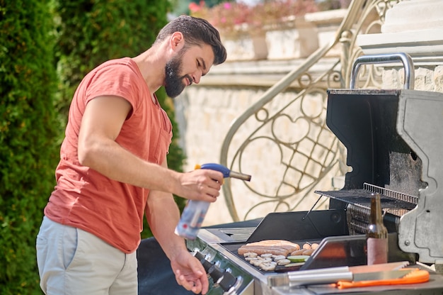 Un homme cuisinant des saucisses et des légumes grillés