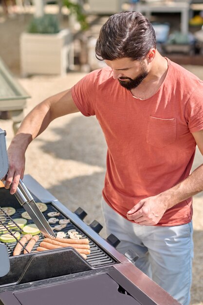 Un homme cuisinant des saucisses et des légumes grillés