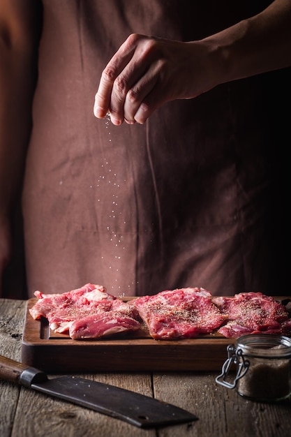 Homme cuisinant des steaks de viande dans la cuisine. Viande de sel et de poivre de chef sur le fond en bois