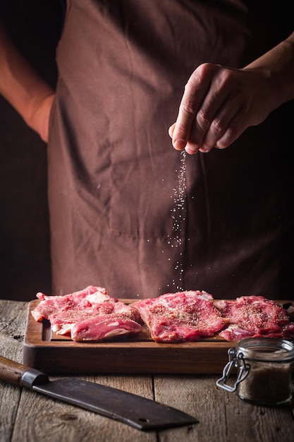 Homme cuisinant des steaks de viande dans la cuisine. Viande de sel et de poivre de chef sur le fond en bois