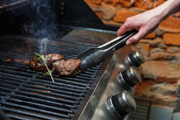 Homme Cuisinant Des Steaks De Viande Sur Un Grill Professionnel à L'extérieur. Main Masculine Avec Des Pinces Tournant Les Biftecks.