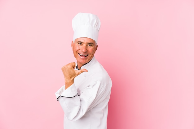 Un homme de cuisinier d'âge moyen pointe le doigt du pouce, riant et insouciant.