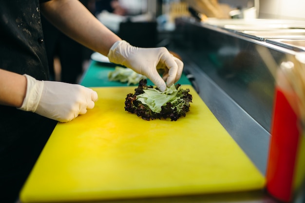 Homme cuisinier prépare une salade fraîche pour hamburger. Processus de préparation du hamburger, cuisson rapide, barbecue