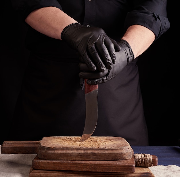 Homme cuisinier en uniforme noir et gants en latex noir est titulaire d'un couteau tranchant vintage sur une planche à découper