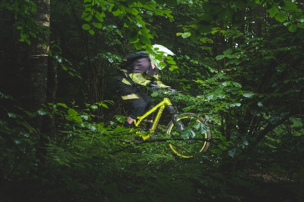 Homme, cycliste dans le casque intégral, balades rapides sur le vélo d'enduro jaune dans la forêt verte