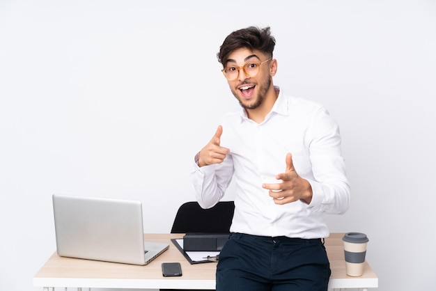 Homme dans un bureau isolé sur mur blanc pointant vers l'avant et souriant