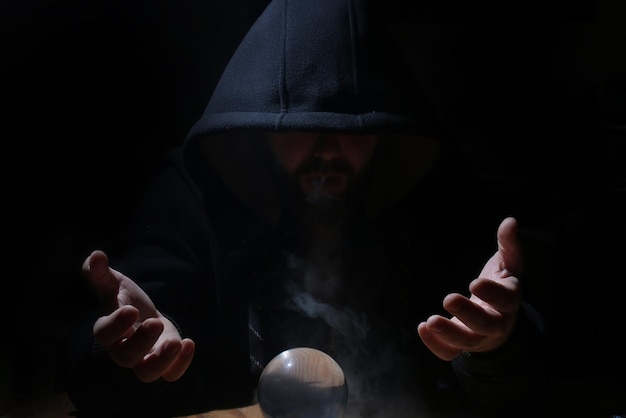 L'homme dans une cagoule noire avec une boule de cristal invoque le mal