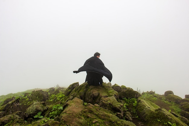 L'homme dans une cape noire se reposant devant un abîme regarde le ciel