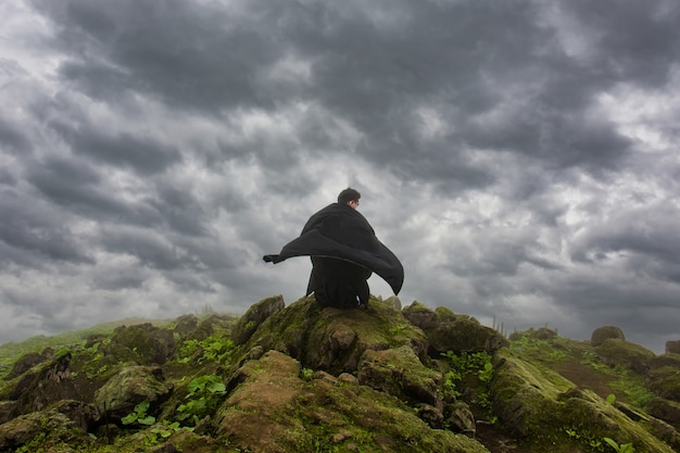 L'homme dans une cape noire se reposant devant un abîme regarde le ciel