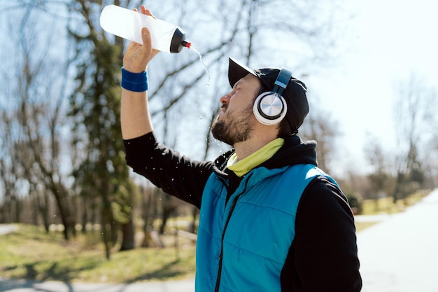 Homme dans une casquette et un casque un athlète un coureur dans une veste sans manches tient une bouteille d'eau