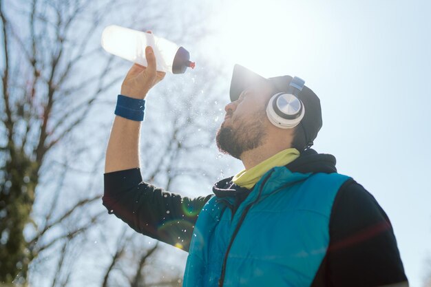 Homme dans une casquette et un casque un athlète un coureur dans une veste sans manches tient une bouteille d'eau