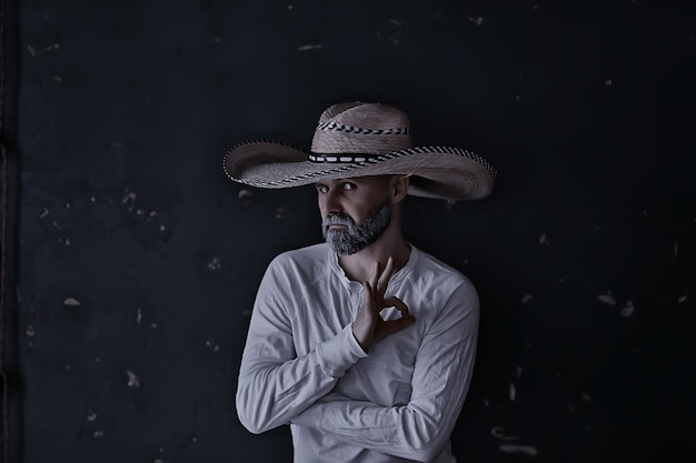 homme dans un chapeau de paille à bord dans les gestes de studio avec ses mains et ses doigts, points. Style sambrero mexique amérique de l'ouest