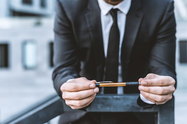 Homme dans un costume d&#39;affaires tient un stylo dans ses mains contre le fond d&#39;un immeuble de bureaux