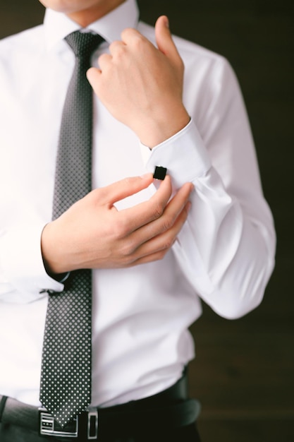 L'homme dans une cravate et un pantalon boutons un bouton de manchette sur la manche d'une chemise blanche