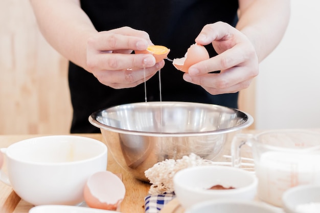 L'homme dans la cuisine cuit une pâte les mains brisent un œuf dans un bol les mains versent un œuf mordu
