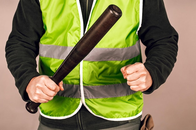 Homme dans un gilet jaune un constructeur ou un manifestant avec une batte de baseball dans ses mains sur un fond gris