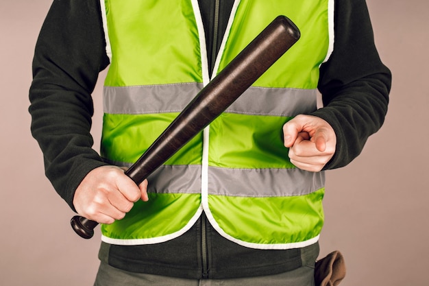 Photo homme dans un gilet jaune un constructeur ou un manifestant avec une batte de baseball dans ses mains sur un fond gris