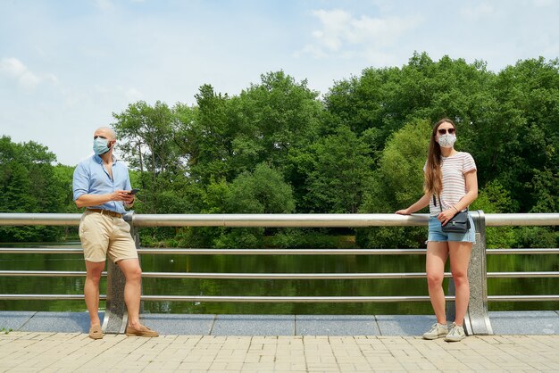 Un homme dans un masque est assis sur un banc en gardant une distance sociale avec une femme