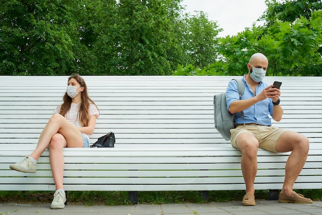 Un homme dans un masque est assis sur un banc en gardant une distance sociale avec une femme