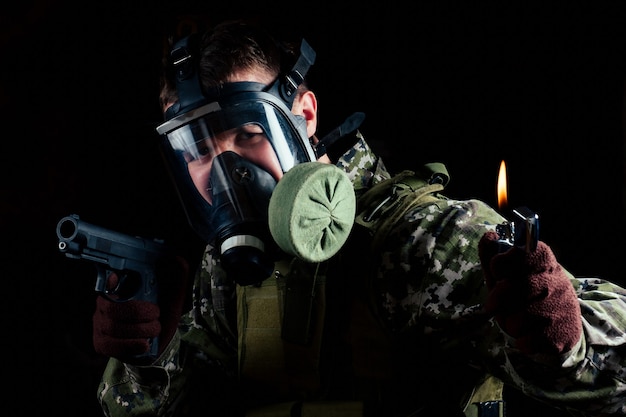 Un homme dans un masque à gaz garde un pistolet et un briquet sur fond noir. La première erreur d'un masque menace.