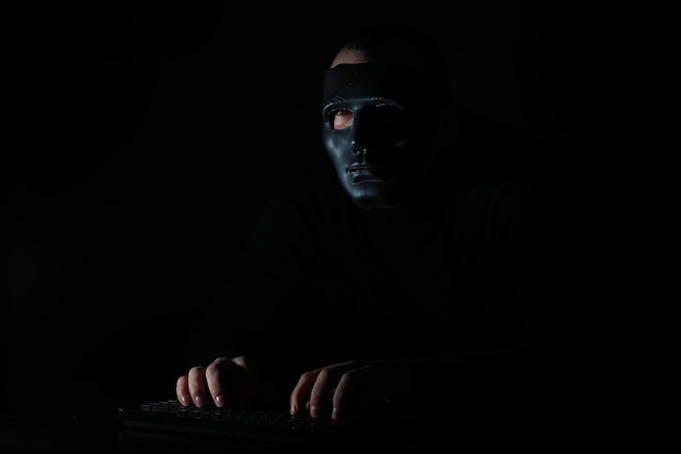 Un homme dans un masque imprime sur le clavier à une table dans le noir