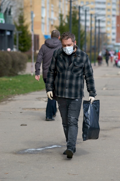 un homme dans un masque médical dans la rue, avec des sacs