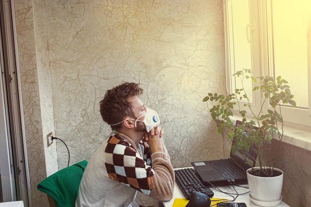 Photo l'homme dans un masque médical travaille dans un ordinateur portable à la maison sur l'auto-isolement