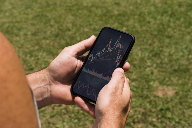 Homme dans le parc tenant un smartphone avec graphique boursier financier sur l'écran Table en bois rustique