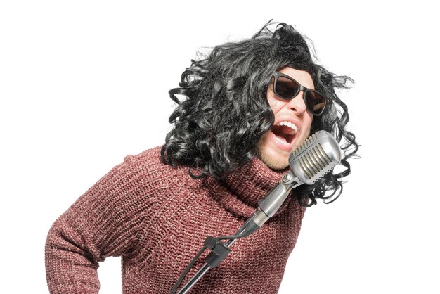 Photo un homme dans une perruque un pull et des lunettes de soleil chantant dans un microphone isolé