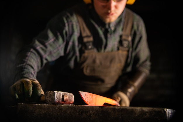 Un homme dans la protection des écouteurs travaillant avec un couteau en métal chaud vierge