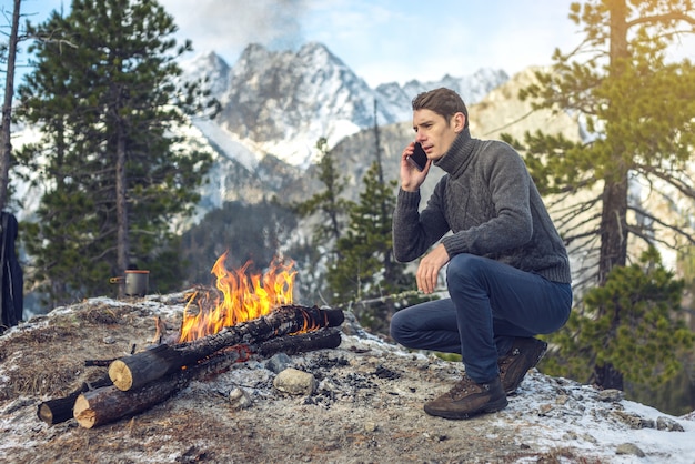 Homme dans un pull, parler au téléphone près d'un feu de camp