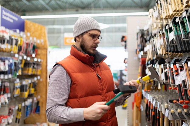 Un homme dans une quincaillerie choisit un marteau pour les réparations