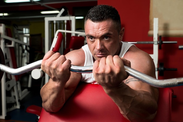 Homme dans la salle de gym exerçant des biceps avec des haltères